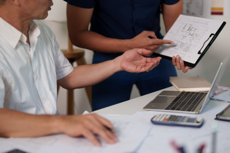 Two engineers analyzing a construction project's blueprint and taking notes on material usage.の写真素材