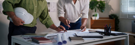 Engineers working together on construction project calculations, using blueprints, laptops, and technical tools at the meeting table.の写真素材