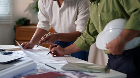 Engineers working together on construction project calculations, using blueprints, laptops, and technical tools at the meeting table.の写真素材
