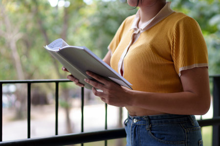 Young Asian woman writing in a notebook while wearing wireless headphones and studying outdoors in a university settingの写真素材