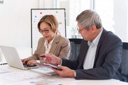 Senior business professionals analyzing financial data together, reviewing reports and discussing investment strategies in a modern office.の写真素材