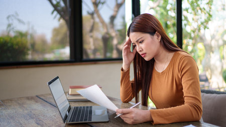 Businesswoman analyzing documents with a stressed expression in a natural-themed office, dealing with work challenges.の写真素材