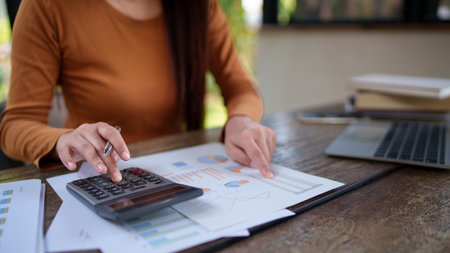 Businesswoman analyzing financial documents at a natural-themed office, focusing on charts and data...