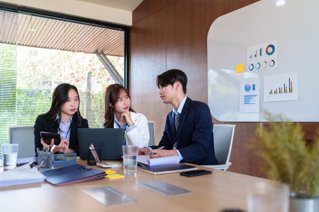 Young startup professionals discussing business data on a laptop, analyzing financial growth and marketing strategies in a modern collaborative workspace for innovative decision-makingの写真素材