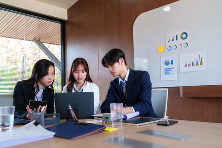 Young startup professionals discussing business data on a laptop, analyzing financial growth and marketing strategies in a modern collaborative workspace for innovative decision-makingの写真素材