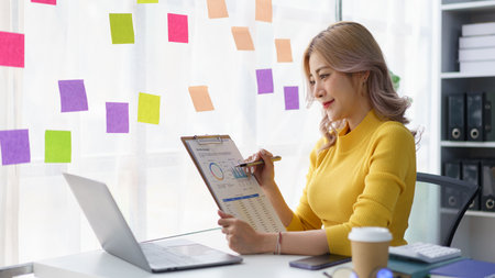 Creative businesswoman brainstorming and writing project ideas on colorful sticky notes at office windowの写真素材