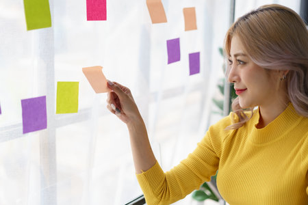 Creative businesswoman brainstorming and writing project ideas on colorful sticky notes at office...