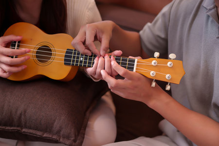 Adult Asian man teaching an Asian adult woman how to play the ukulele with guidance. Hands on...