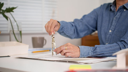 Adult Asian man's hands using a compass to create new architectural design blueprint of a house....