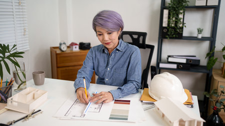 Asian older woman architect is designing blueprints home interior floor plan and modeling for house development architecture project concept. Architect design for building construction project with design floorの写真素材
