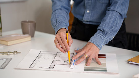 Adult Asian architect's hands meticulously drafting a blueprint. Focusing on blueprint details for a...