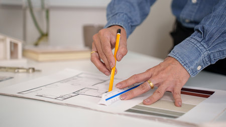 Older architect's hands drawing a blueprint using a ruler and pencil. Focus on the architectural...