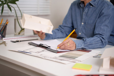Older adult architect drawing blueprint design, reviewing home construction blueprint plans for...