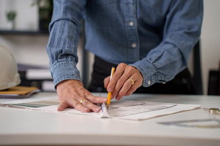 Close-up of architect hands drawing blueprint on a white table. An adult architect is working and creating detailed plans blueprint for a building design project with precision and care. Architect hands drawing blueprint for success.の写真素材