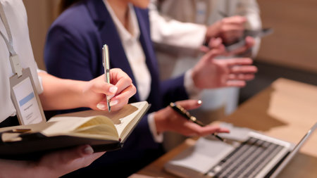 Close up of adult Asian women's hands at a business meeting writing notes in a notebook with a pen. Brainstorming teamwork in an office space discussing ideas and planning strategy.の写真素材