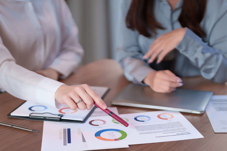 Adult Asian women analyzing financial data, charts, and sales reports at a business meeting. Collaboration and teamwork using a laptop on the table. Analyzing Business Graphs.の写真素材