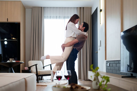 A happy Asian adult couple shares a loving moment in their home The man lifts the woman in his arms with joy expressing their relationship love affection and commitment.の写真素材