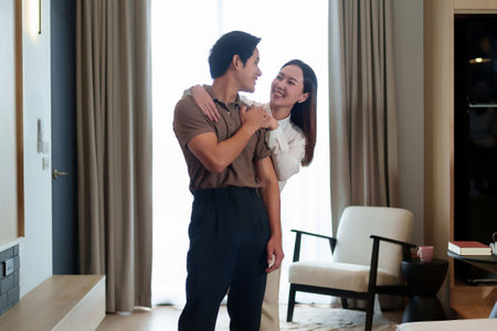 This heartwarming image shows a young Asian couple embracing tenderly in their modern living room Capturing love happiness and the simple joys of being together Home interior is elegantの写真素材