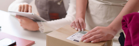 Adult Asian women are preparing a package for delivery while using a tablet for a small business at...