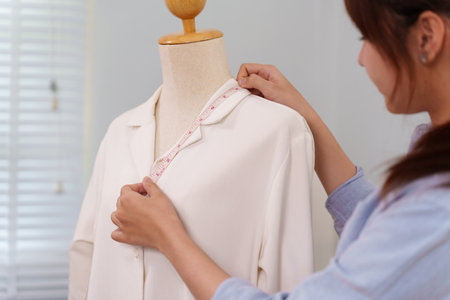 Adult Asian woman measures a shirt with tape measure on a mannequin. This is a fashion design small...