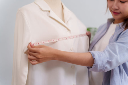 An Asian adult woman is using a measuring tape on the dress form to measure the size of the clothes. She is designing and working on a new collection.の写真素材