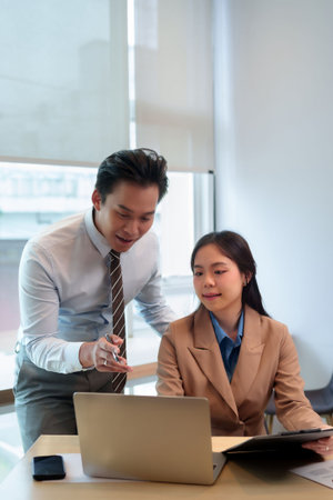 Young Asian man woman professionals discuss business analysis project strategy using laptop clipboard office meeting roomの写真素材