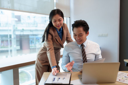 Asian business man woman collaborate office meeting reviewing financial report using laptop discussing strategy futureの写真素材