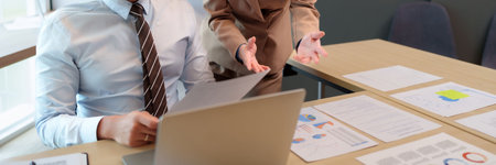 Two Asian business professionals discuss financial data and market reports during a meeting in a...