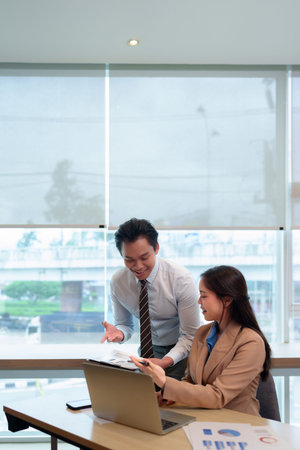 Asian business adults collaborate analyze data reports discuss project plans modern office environment near window workspace teamwork togetherの写真素材
