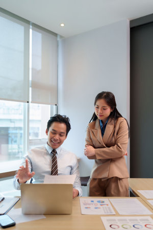 Asian business adults discuss reports in modern office analyze data collaborate on strategy plan business growth teamwork partnership togetherの写真素材