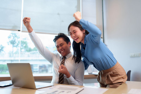 Two Asian professional adults show excited triumphant happy expression successful moment completing achieving goal reviewing data analysis in office environmentの写真素材