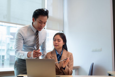 Professional Asian adults collaborate discuss business strategy using laptop computer during office meeting successful teamwork environmentの写真素材
