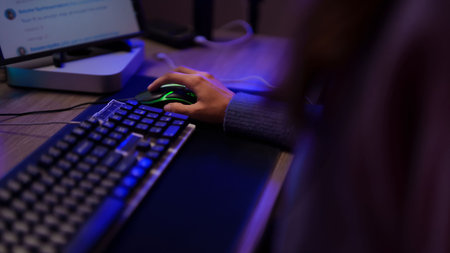 Adult hand operates illuminated gaming mouse computer setup dimly lit desk surface close view focus on actionの写真素材