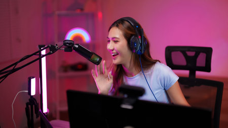Happy Asian woman streamer engages audience with professional microphone headphones setup creating...