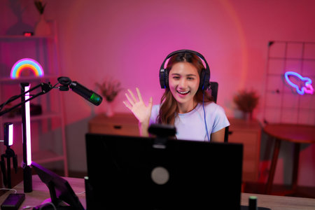 Asian woman streams online home room setup Happy young adult female broadcasts gaming content laptop...