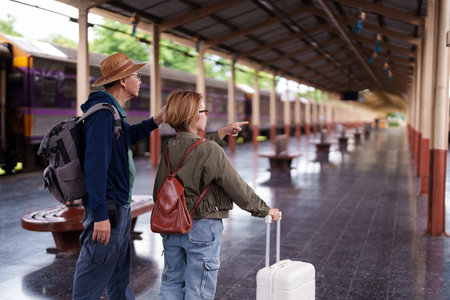 Senior couple stands on train platform pointing looking waiting for journey adventure transportation travel exploring retirement life togetherの写真素材