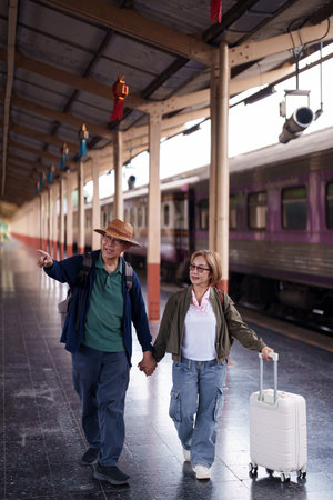 Happy older Asian couple travels exploring destination train station platform vacation retirement...