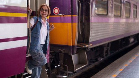 Happy older Asian woman traveler standing by train door public transport platform leisure travel...