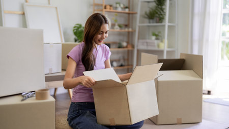 Asian young woman packing belongings in cardboard boxes at home to move out or relocation to new...