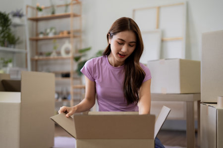 An Asian young adult woman is unpacking moving boxes at her new home or apartment Relocating and...