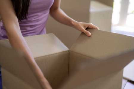 Adult Asian women prepare belongings in cardboard boxes for relocation and moving to a new home to...