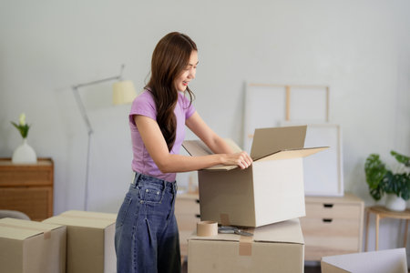 Young Asian woman preparing boxes for moving to a new apartment. She is unpacking her stuff after...