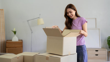 Young Asian woman smiles while unpacking boxes in her new home Celebrating her new beginning after...