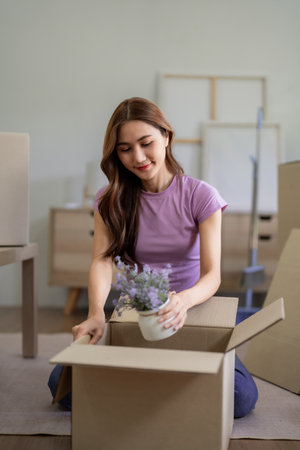 Adult Asian woman carefully packing a flower pot into a cardboard box for her move to a new home....