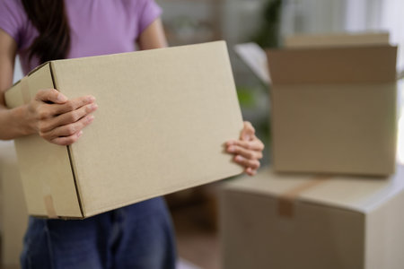 This image shows an Asian woman carrying a box during a move. She is relocating to a new home with...