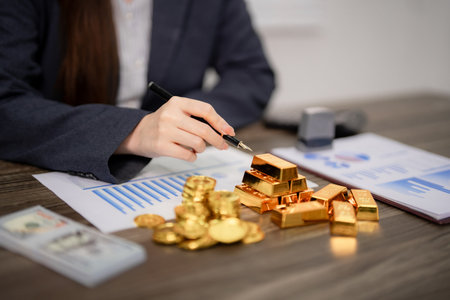 Adult Asian business hand reviews gold bars coins financial charts currency for smart investment decisions and wealth managementの写真素材