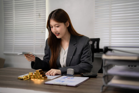 Adult Asian woman plans gold investment strategy manages wealth on office desk analyzes finances for prosperous future professional asset growthの写真素材