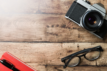 Old camera on a wooden table with glasses and red notebookの写真素材