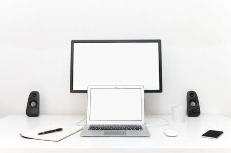 Clean desktop with a laptop and external screen next to a phone and a notepadの写真素材