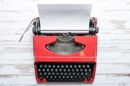 Red vIntage typewriter on a wooden desk with a plain paper loaded inの写真素材